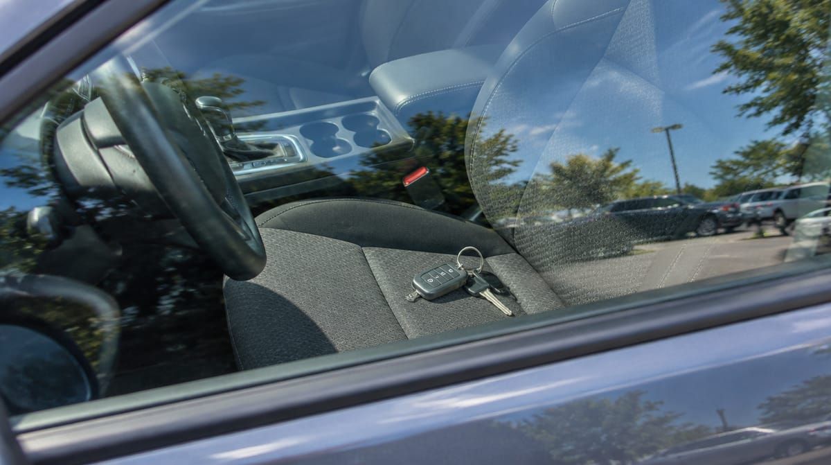 A key fob and key on the driver’s seat, seen through a closed car window