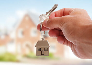 Holding house keys on house shaped keychain in front of a new home